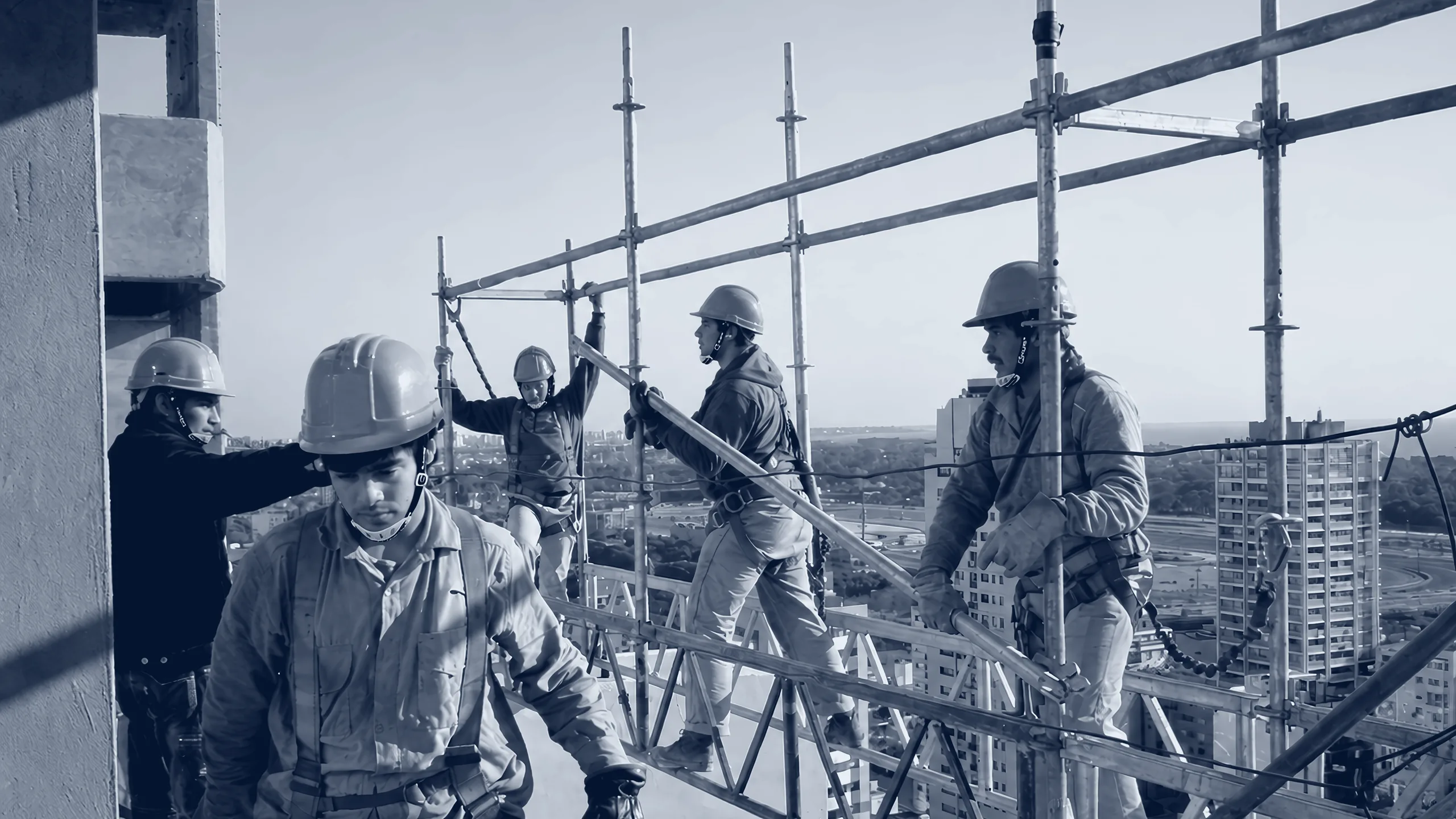 Cinco operarios con casco y arnés sobre una estructura tubular en altura, con edificios de la ciudad de fondo